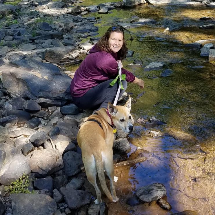 Picture of the author by a stream with her dog