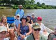 A group of smiling people, many wearing hats on a boat ride