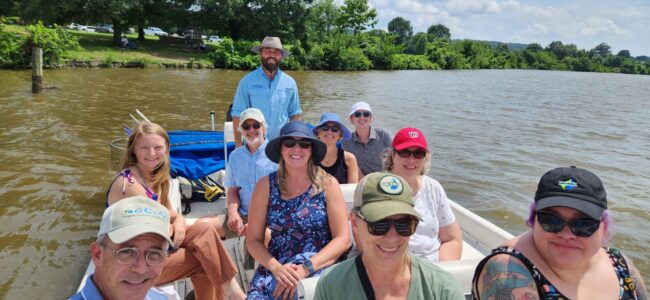 A group of smiling people, many wearing hats on a boat ride