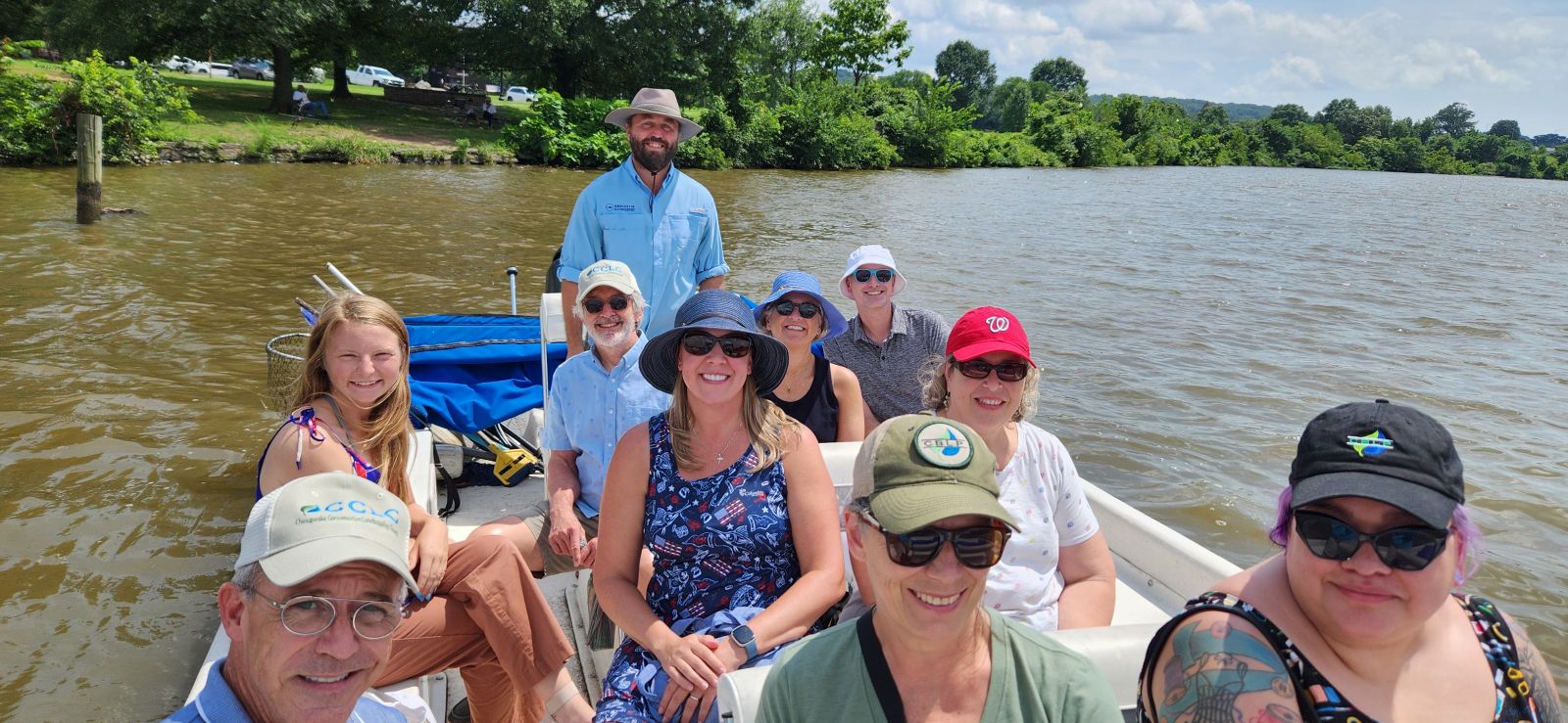 A group of smiling people, many wearing hats on a boat ride