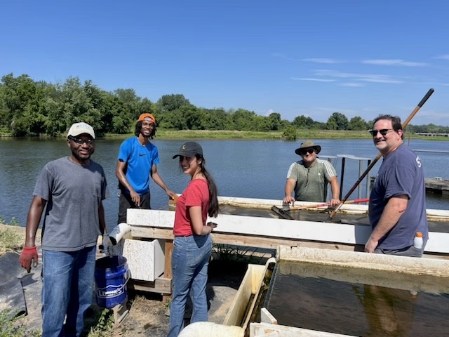 Five smiling people stand around the Turf Scrubber in front of the river.